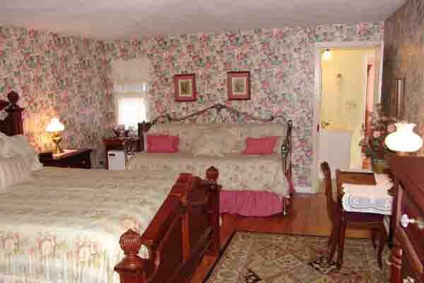A Gettystown Inn bedroom with floral wallpaper, a wooden bed and warm bedside lamps.
